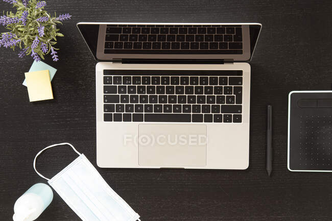 From above of laptop placed on black table near protective mask and bottle of antiseptic — Foto stock