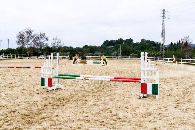 Barrières sautantes avec poteaux rayés installés sur l'arène de dressage sablonneuse de l'école équestre dans la campagne — Photo de stock