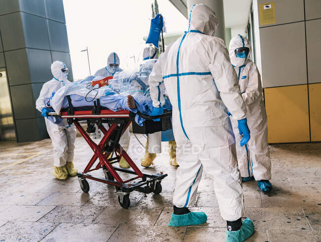 Vue arrière d'un groupe anonyme de médecins professionnels en combinaison de protection transportant un patient infecté par le virus à l'hôpital — Photo de stock