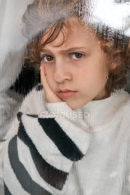 Bored boy looking out wet window — Stock Photo