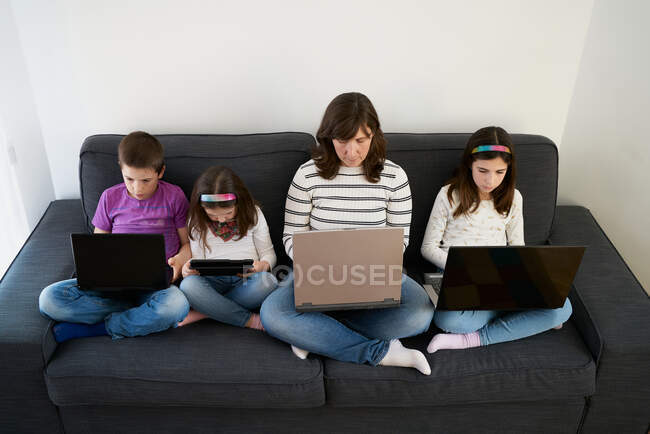Sérieux mère et les enfants passent du temps ensemble en utilisant des gadgets sur le canapé à la maison — Photo de stock