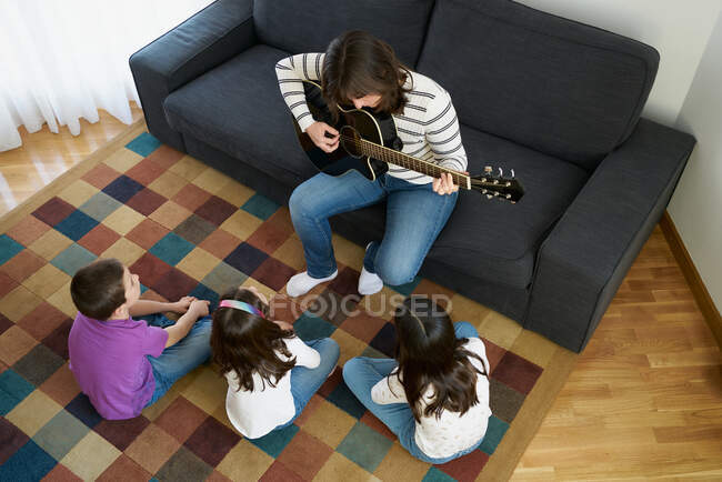 Женщина играет на гитаре для детей в гостиной дома — стоковое фото