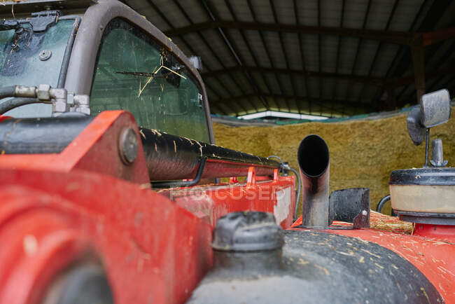 Cab and exhaust tube of shabby red tractor parked in garage on farm yard near hay stacks — Foto stock