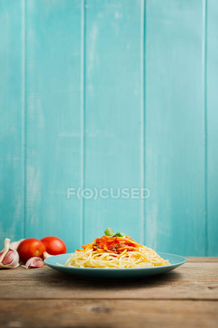 Assiette en céramique bleue avec pâtes et sauce tomate décorée de persil sur une table en bois avec fond en bois bleu clair — Photo de stock