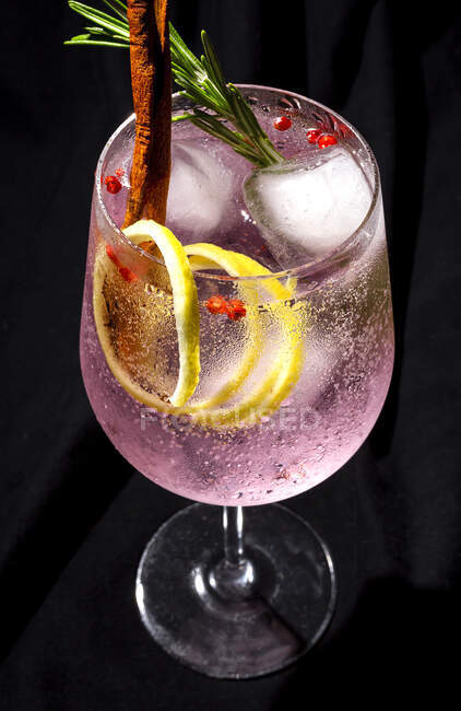 Cóctel de Gin tonic con agua tónica rosa, pimienta rosa, romero, menta, canela, limón y naranja sobre fondo oscuro - foto de stock