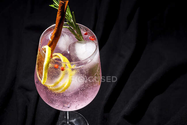 Gin tonic cocktail with pink tonic water, pink pepper, rosemary, mint,cinnamon,lemon and orange on dark background — Stock Photo