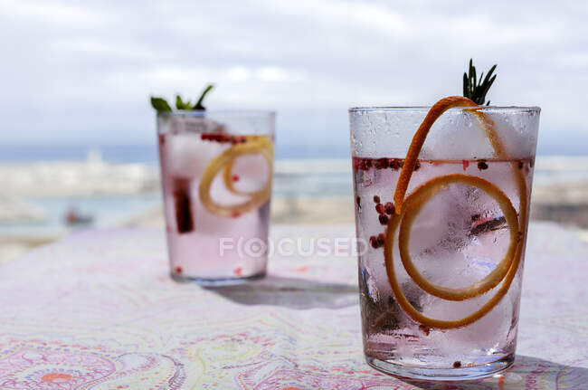 Gin tonic cocktail with pink tonic water, pink pepper, rosemary, mint,cinnamon,lemon and orange in the sunlight on a restaurant table — Stock Photo