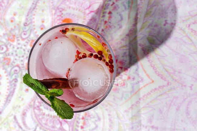 Gin tonic cocktail with pink tonic water, pink pepper, rosemary, mint,cinnamon,lemon and orange in the sunlight on a restaurant table — Stock Photo