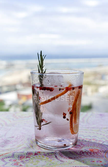 Gin Tonic Cocktail mit rosa Tonic Wasser, rosa Pfeffer, Rosmarin, Minze, Zimt, Zitrone und Orange im Sonnenlicht auf einem Restauranttisch — Stockfoto