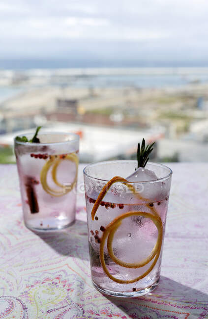 Cocktail tonico al gin con acqua tonica rosa, pepe rosa, rosmarino, menta, cannella, limone e arancia alla luce del sole su un tavolo da ristorante — Foto stock