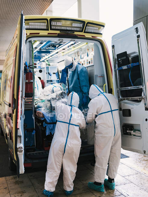 Gruppo di medici professionisti in uniforme protettiva in piedi in ambulanza con attrezzature e preparazione per il trasporto del paziente — Foto stock