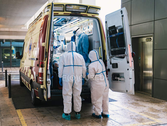 Grupo de médicos profesionales en uniforme de protección de pie en coche ambulancia con el equipo y la preparación para el transporte del paciente - foto de stock