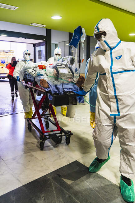 Анонімні групи професійних лікарів у білій захисній формі транспортують пацієнта на шарнір до операційної кімнати. — стокове фото