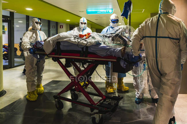 Groupe anonyme de médecins professionnels en uniforme de protection blanc transportant le patient sur le brancard à la salle d'opération — Photo de stock