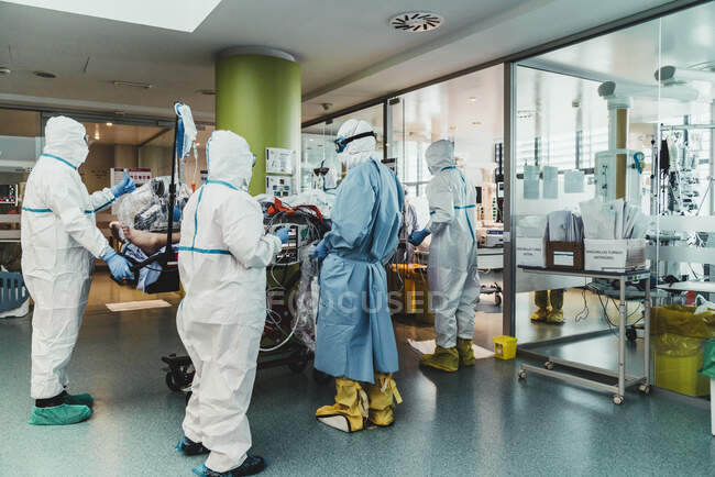Неузнаваемые профессиональные врачи в защитной форме и масках, ухаживающие за пациентом с вирусной инфекцией, стоя в операционной в современной больнице — стоковое фото