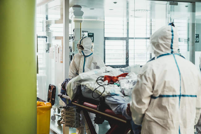 Нерозпізнані професійні лікарі в захисній формі та масках, які доглядають за пацієнтом з вірусною інфекцією, стоячи в операційній кімнаті в сучасній лікарні. — стокове фото