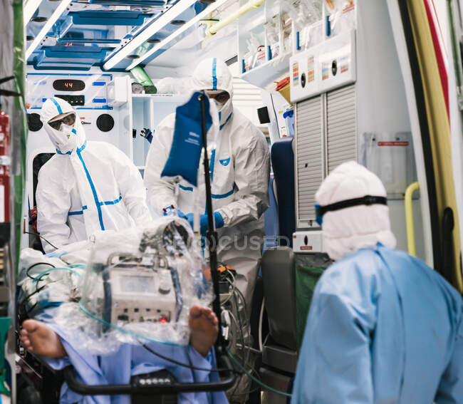 Group of professional doctors in protective uniform standing in ambulance car with equipment and preparing for patient transportation — Stock Photo