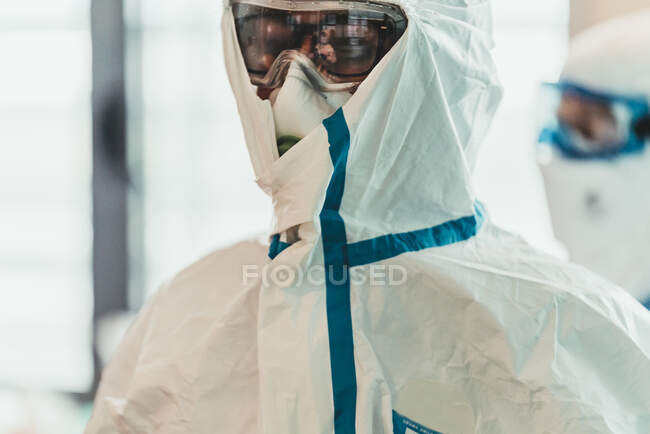 Серйозний професійний лікар в захисній формі та масці, що стоїть в сучасній операційній кімнаті — стокове фото
