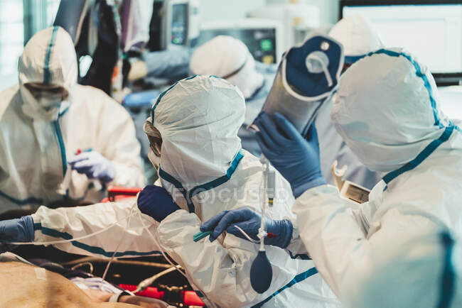 Grupo de médicos profissionais vestindo máscaras protetoras e ternos de pé perto da mesa de operação com equipamentos e se preparando para a operação na clínica moderna — Fotografia de Stock