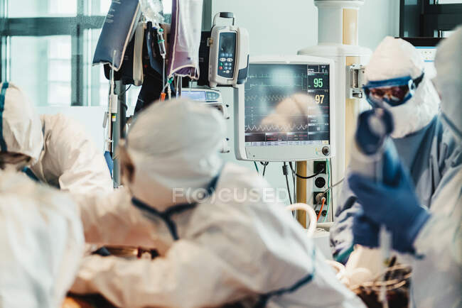 Groupe de médecins professionnels portant des masques de protection et des costumes debout près de la table d'opération avec de l'équipement et se préparant pour l'opération dans une clinique moderne — Photo de stock