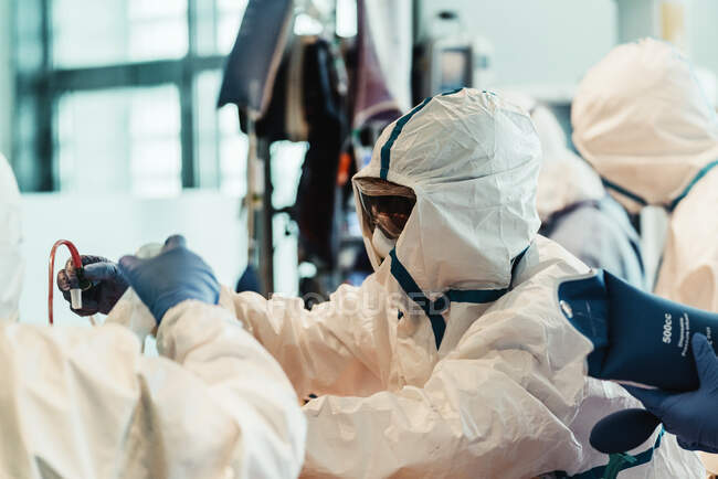Група професійних лікарів у захисних масках та костюмах стоїть біля операційного столу з обладнанням та готується до експлуатації в сучасній клініці — стокове фото