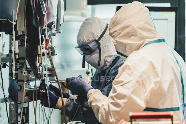 Visão lateral de médicos profissionais em máscaras e uniformes de proteção verificando equipamentos antes da operação no hospital moderno durante a epidemia — Fotografia de Stock
