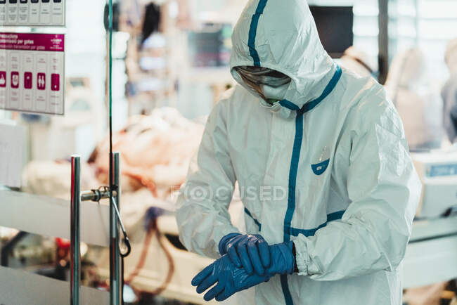 Medico professionista in uniforme bianca protettiva e maschera che indossa guanti di lattice prima dell'operazione nella moderna sala operatoria in ospedale — Foto stock