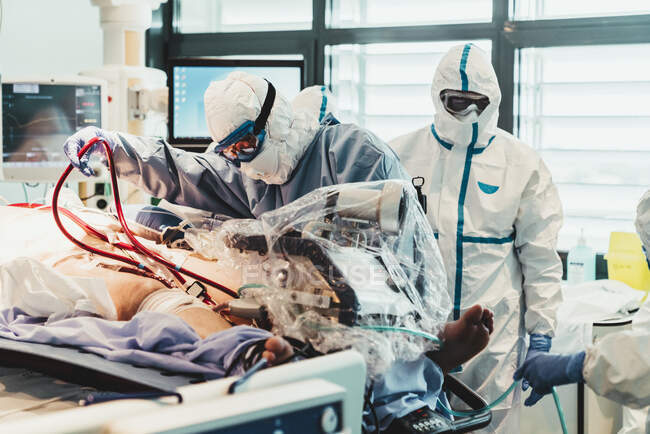 Unerkennbare Berufsärzte in Schutzuniformen und Masken kümmern sich im Operationssaal eines modernen Krankenhauses um einen Patienten mit Virusinfektion — Stockfoto
