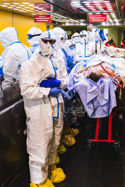 Groupe de médecins anonymes en uniforme de protection et masque debout autour du patient avec infection virale dans l'ascenseur à l'hôpital — Photo de stock