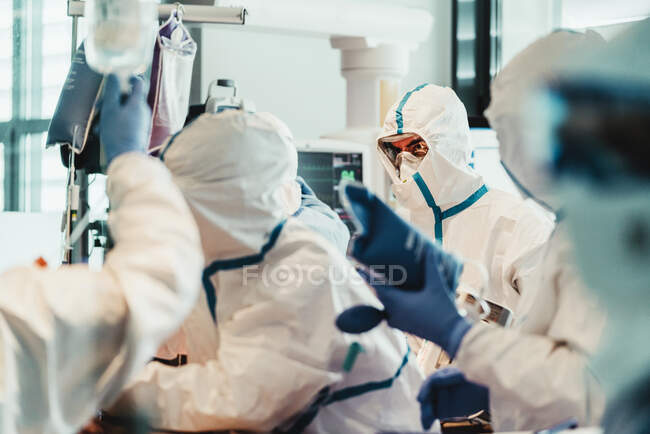 Gruppo di medici professionisti che indossano maschere protettive e tute in piedi vicino al tavolo operatorio con attrezzature e si preparano per l'operazione nella moderna clinica — Foto stock