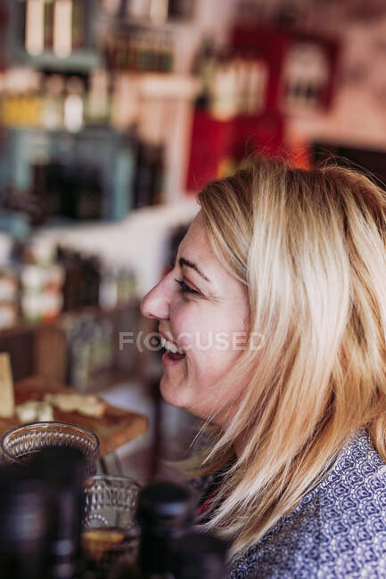 Vista laterale di felice donna bionda costumista con tazza di vetro degustazione di vino durante lo shopping nel negozio di gastronomia locale — Foto stock