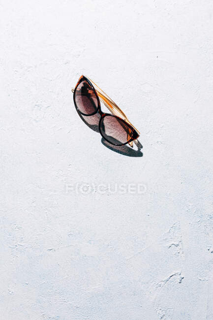 De dessus les lunettes de soleil à la mode placées sur la surface rugueuse de stuc par une journée ensoleillée pendant les vacances d'été — Photo de stock