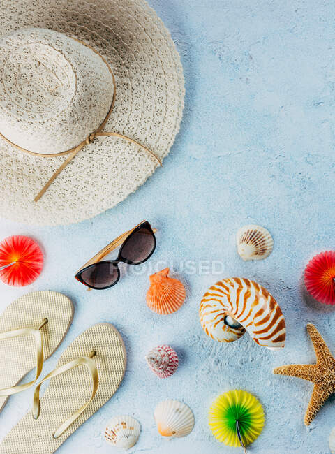 Draufsicht auf verschiedene Muscheln in der Nähe bunter Cocktaildekorationen und stilvoller Sommer-Accessoires auf blauem Putz — Stockfoto