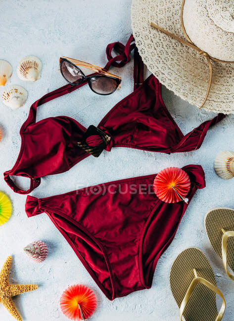 Red swimwear with stylish accessories placed on plaster surface near seashells and cocktail decorations on plaster surface — Stock Photo