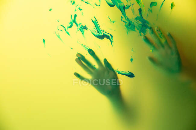 Crop artesana con las manos pintadas de pie detrás de la pared de color amarillo translúcido con pinceladas - foto de stock