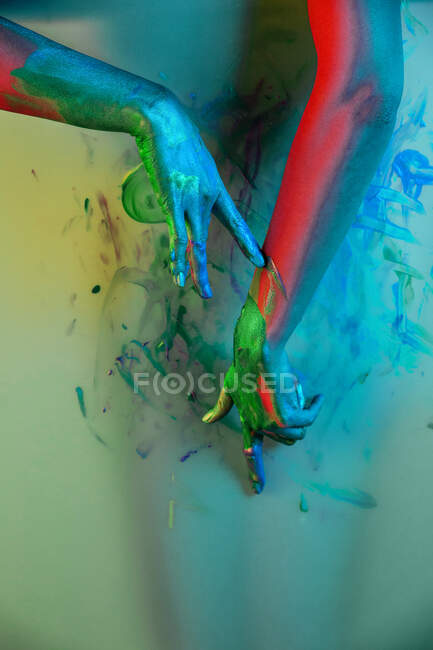 Recorte artista femenina irreconocible mancha pared colorida con pintura en el fondo colorido gradiente en el estudio - foto de stock