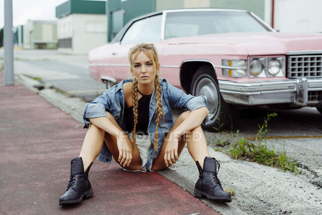 Attraktives blondes Mädchen sitzt auf dem Bürgersteig in der Nähe eines rosa Oldtimers — Stockfoto