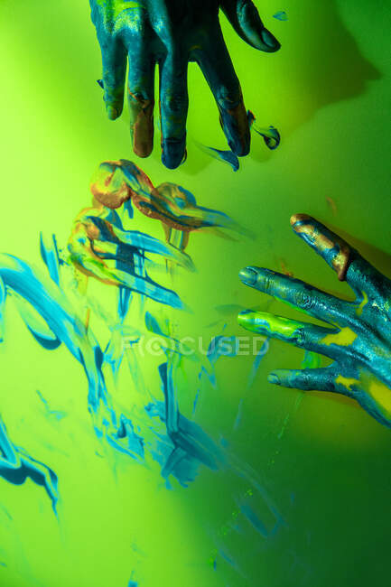 Crop artesana con las manos pintadas de pie detrás de la pared de color amarillo translúcido con pinceladas - foto de stock
