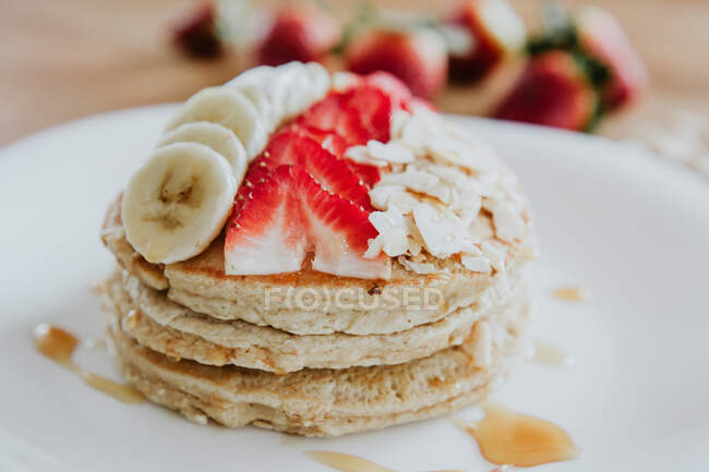 Closeup stack of yummy pancakes with pieces of banana and strawberry served on plate with almond flakes and honey during breakfast — Stock Photo