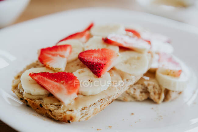 Sanduíches deliciosos de banana e morango com purê doce colocado na placa durante o café da manhã na mesa de madeira — Fotografia de Stock