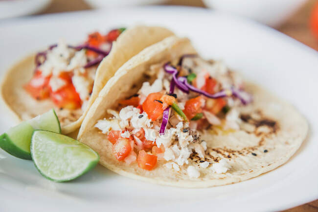 Dall'alto deliziosi appetitosi tacos messicani con ripieno di verdure serviti con fette di lime verde sul piatto sul tavolo — Foto stock