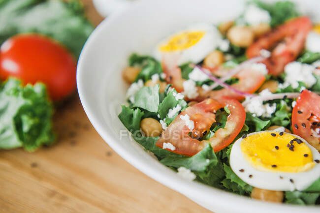 Bowl of tomato and lettuce salad with chickpeas and boiled eggs placed on lumber table near silverware and sauce — Stock Photo