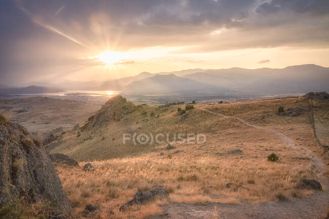 Bright sun setting on cloudy sky over grassy hills in calm evening in Spain — Stock Photo