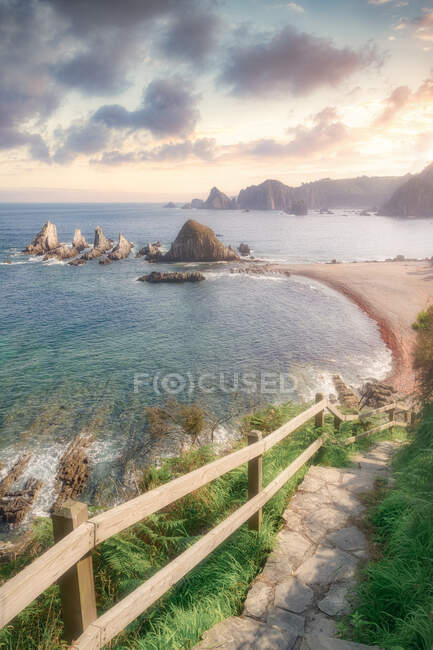 Sentier rocheux étroit avec rampe en bois allant sur la côte près de la mer calme pendant le coucher du soleil dans la soirée nuageuse en Espagne — Photo de stock