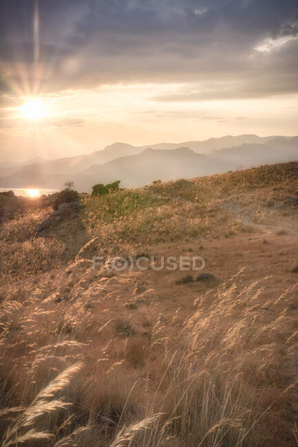 Bright sun setting on cloudy sky over grassy hills in calm evening in Spain — Stock Photo