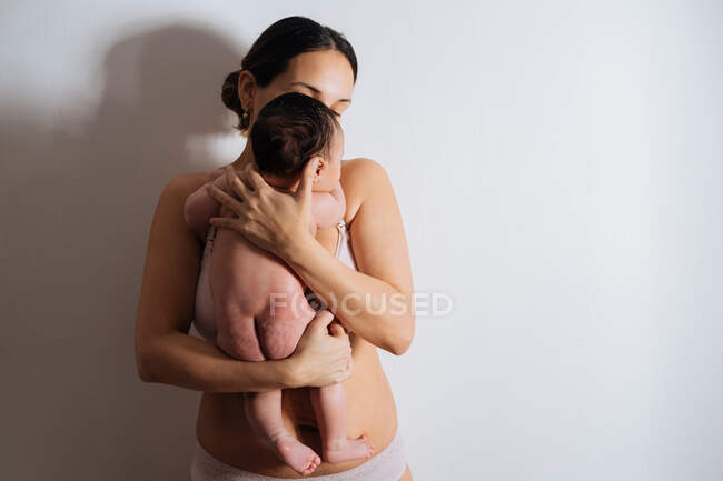 Happy young mother in bra holding cute little baby on hands in white light room — Stock Photo