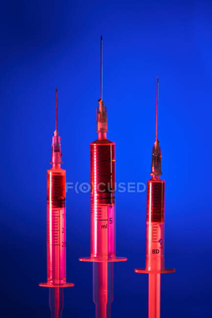 Set di poche siringhe mediche riempite con nuovi farmaci vaccinali composti posti su superficie riflettente in luce rossa su fondo blu — Foto stock
