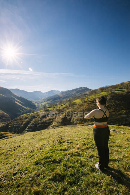 Rückenansicht einer anonymen Frau, die barfuß auf dem grünen Gras eines Hügels steht und an sonnigen Tagen in Kantabrien Yoga praktiziert — Stockfoto
