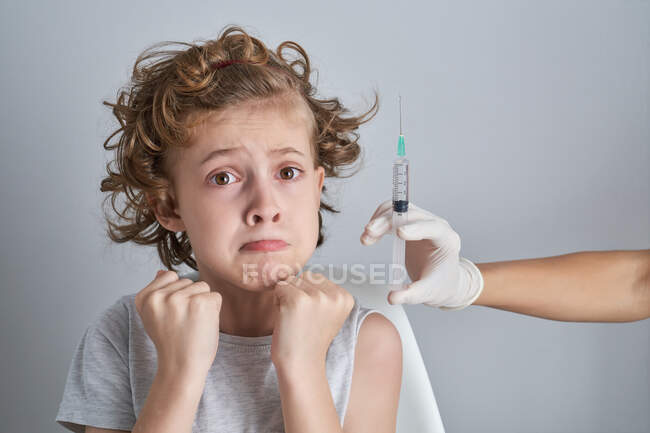 Médico de cosecha irreconocible en guantes de látex que llena la jeringa con medicamentos de la vacuna del frasco que se prepara para la inyección en el hombro del niño con el pelo rizado - foto de stock