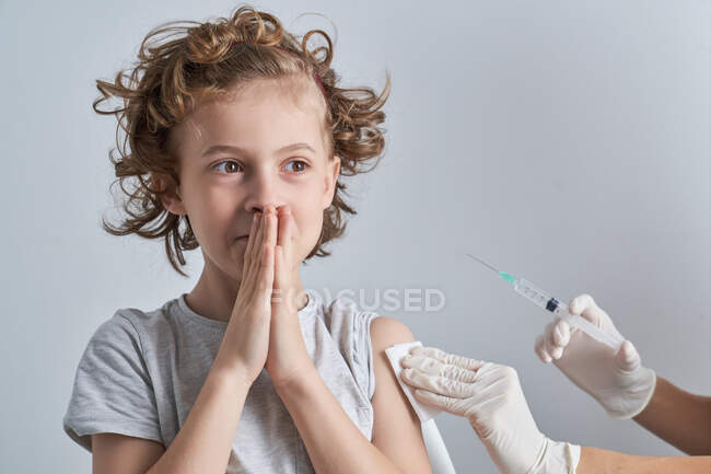 Médico de cosecha irreconocible en guantes de látex que llena la jeringa con medicamentos de la vacuna del frasco que se prepara para la inyección en el hombro del niño con el pelo rizado - foto de stock